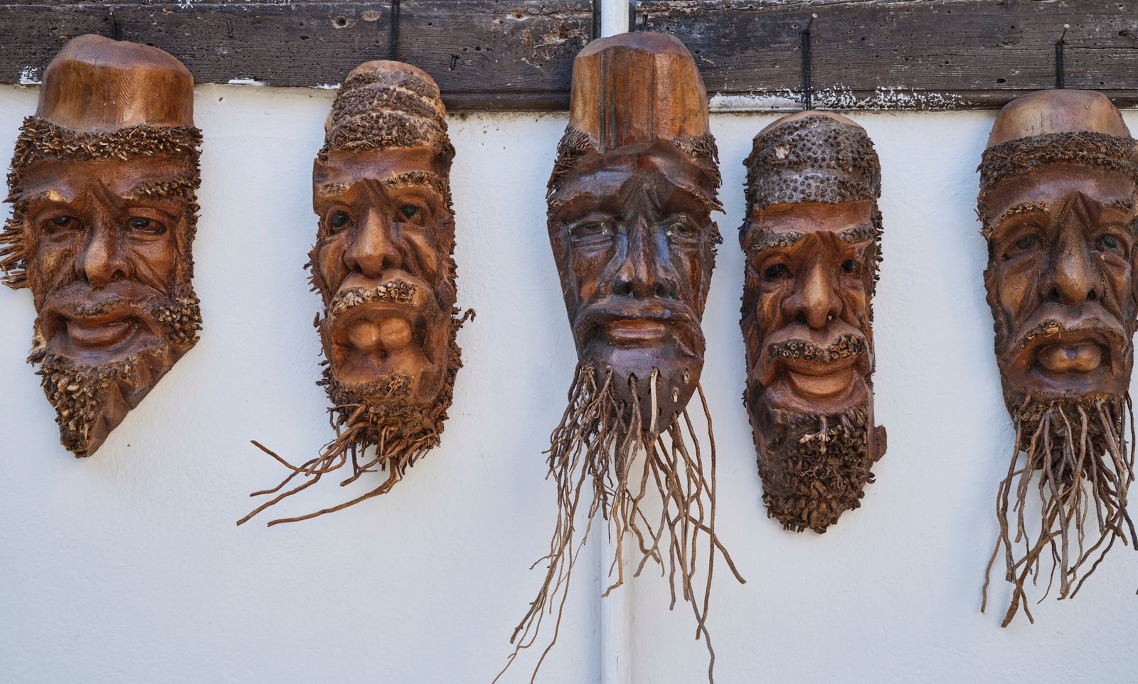 A set of handmade carved wooden masks hanging on a wall
