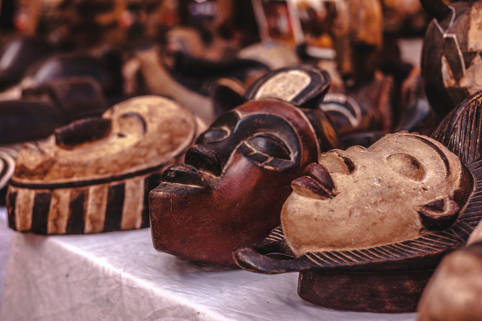 Carved wooden masks laid out on a table for sale, with a light faced mask in focus