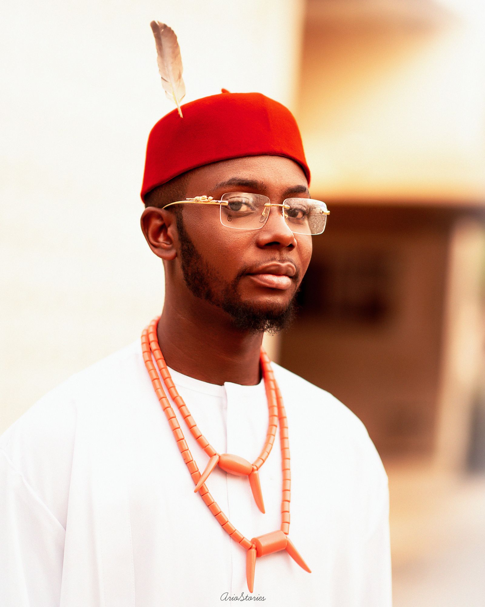 Portrait of a man in traditional Igbo attire with a red cap and beads