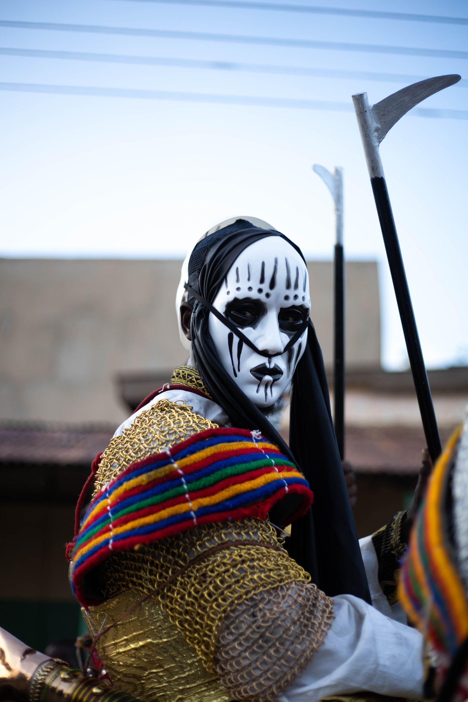 Masked performer in a white face mask and woven costume at a festival in Nigeria